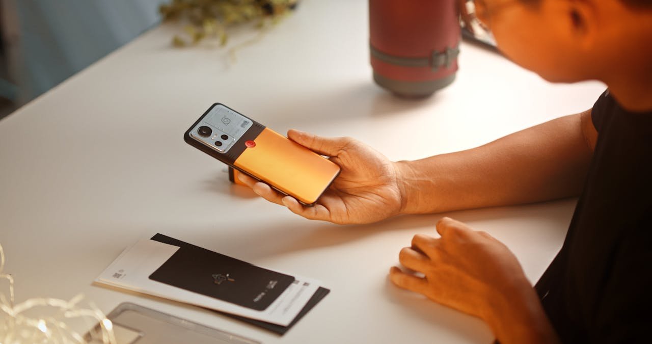 Close-up of a person holding a modern smartphone with a vibrant orange case at a desk.