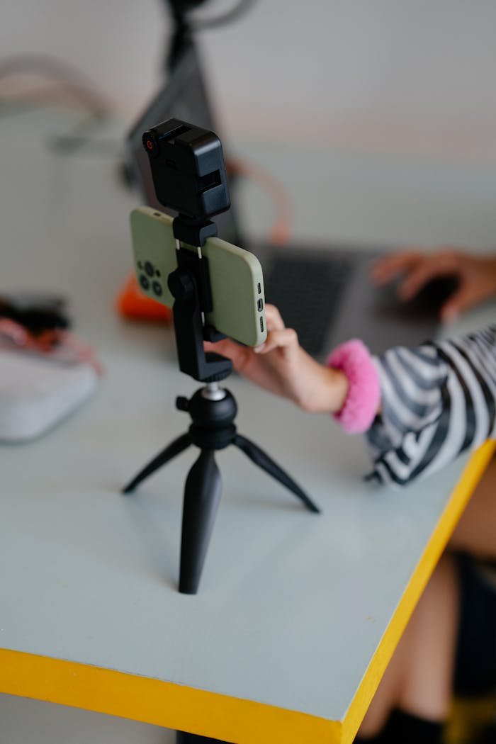 Close-up of woman adjusting smartphone on tripod while working at a desk, blending technology and productivity.