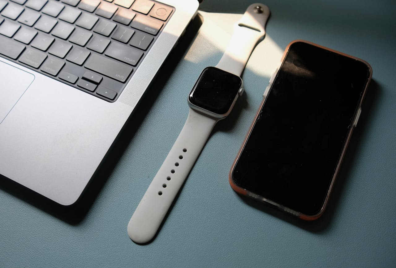 Flat lay of a laptop, smartwatch, and smartphone on a blue surface, highlighting modern technology.